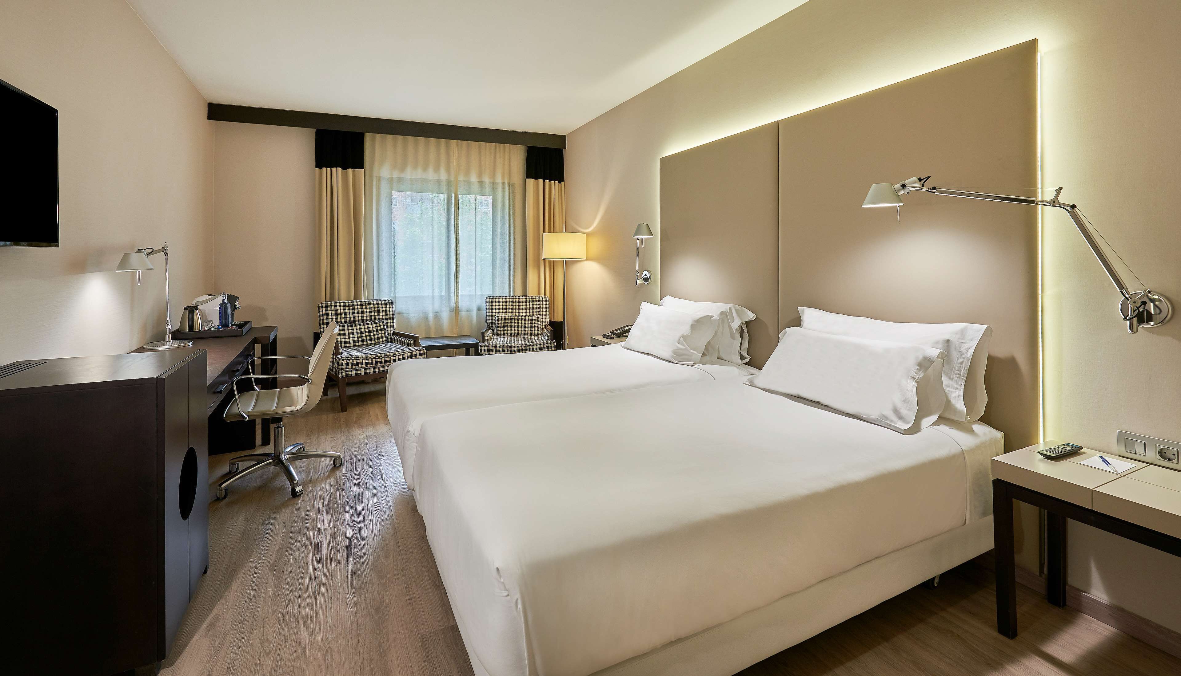 A hotel room with a large bed, a desk with a lamp, a chair, and a TV.