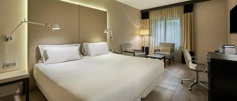 A hotel room with a large bed, two bedside tables, a desk with a chair, a lamp, and a window with curtains.