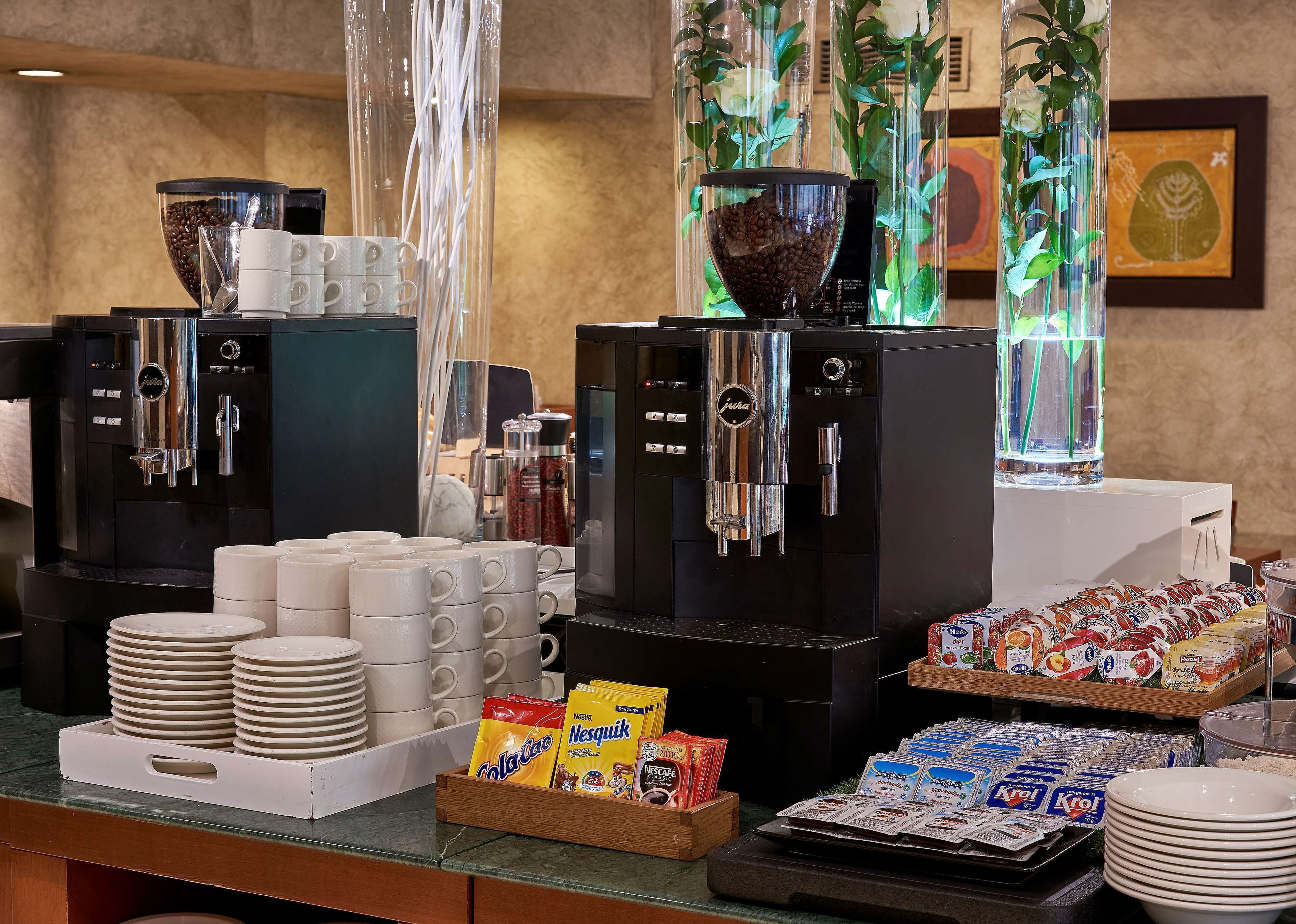 A coffee station with multiple espresso machines, coffee cups, and a variety of coffee pods.