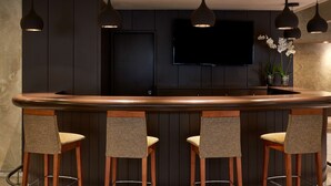 Un coin bar avec quatre tabourets, un téléviseur à écran plat fixé au mur et des luminaires suspendus.