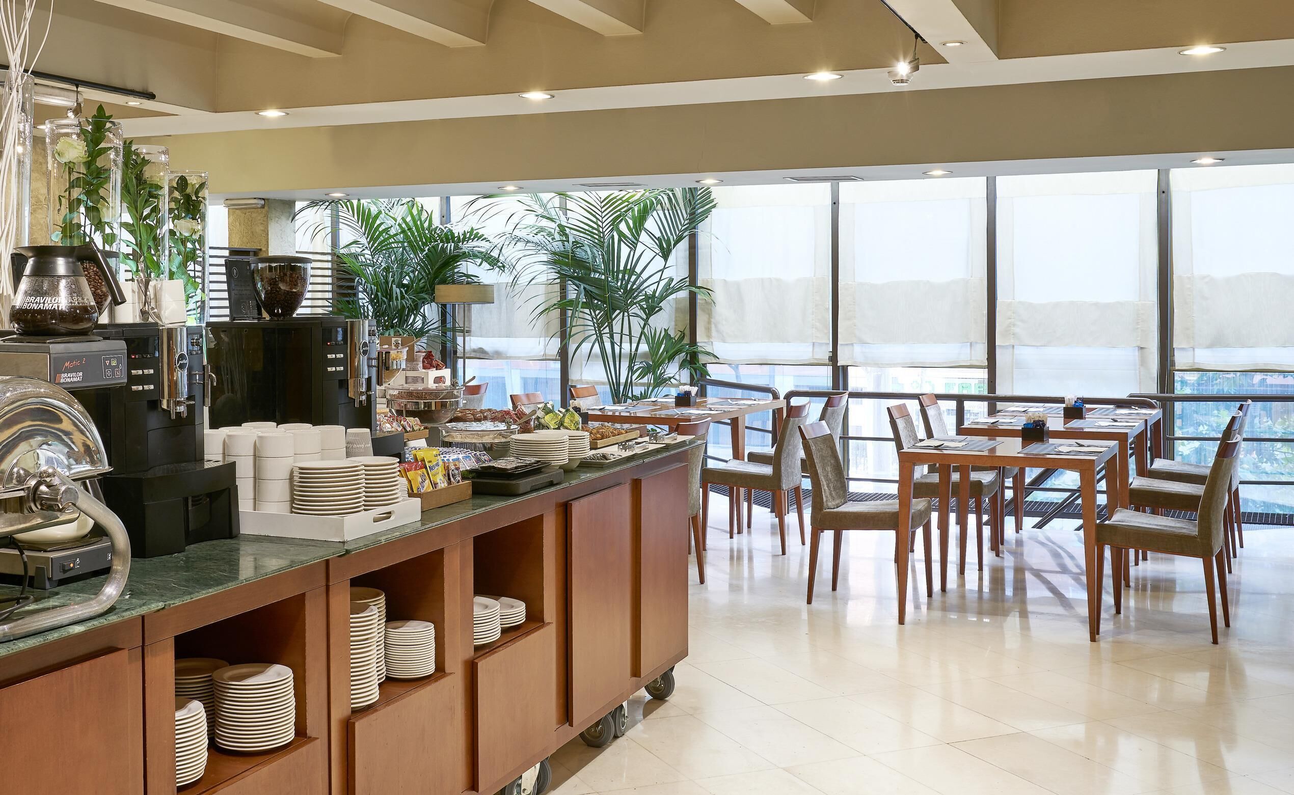 A modern breakfast bar with coffee machines, a variety of food items, and a seating area with a view.