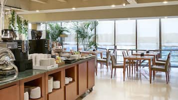 A modern breakfast bar with coffee machines, a variety of food items, and a seating area with a view.
