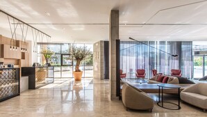 A spacious lobby with a modern design, featuring a large potted tree, comfortable seating areas, and large windows providing natural light.