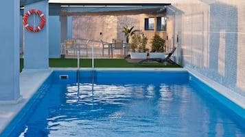 Una piscina al aire libre, sombrillas, sillones reclinables de piscina