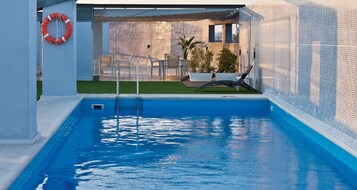 Una piscina al aire libre, sombrillas, sillones reclinables de piscina