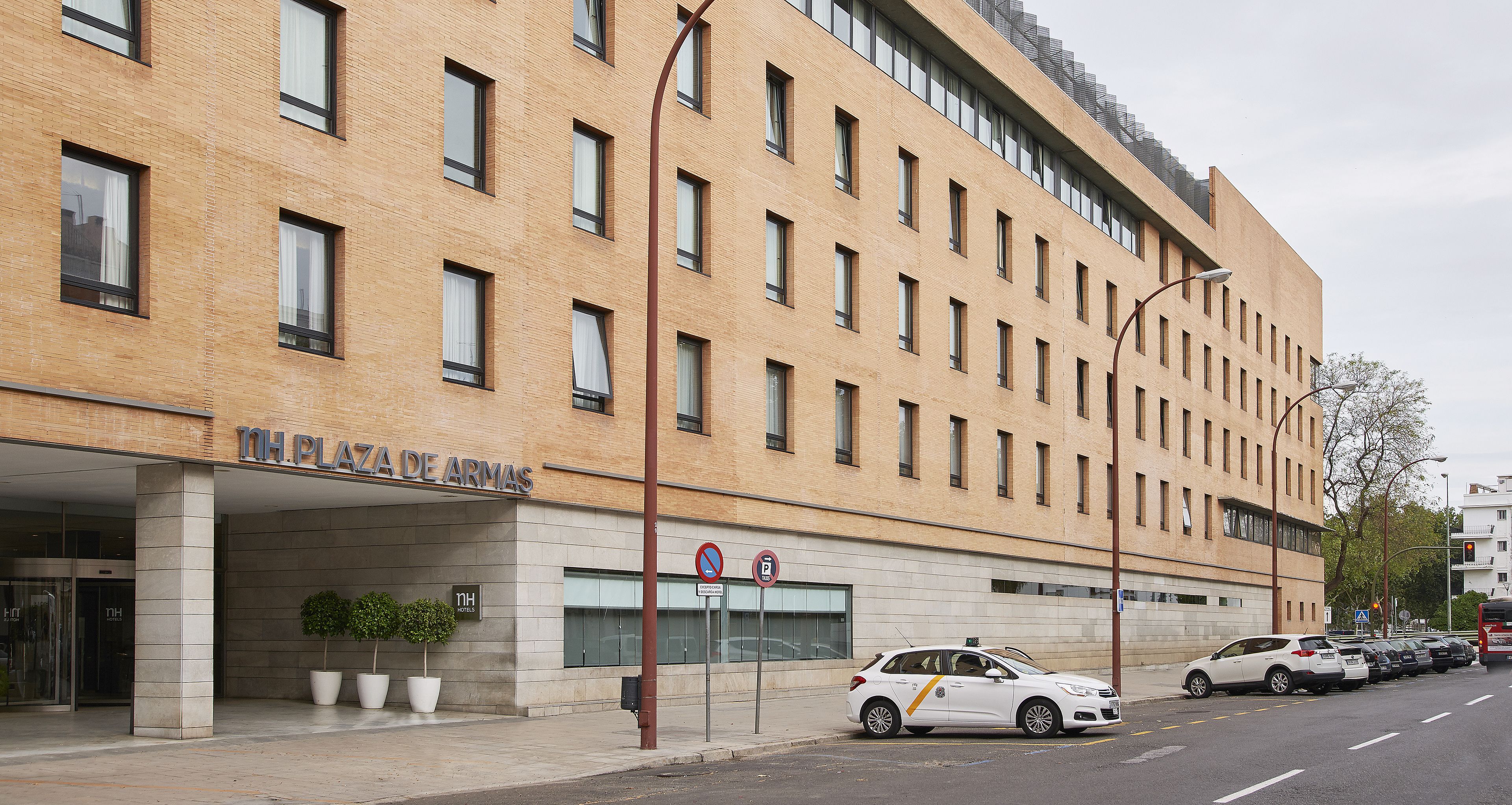 Un hotel de varios pisos con fachada moderna, un acceso cubierto y un estacionamiento con coches.