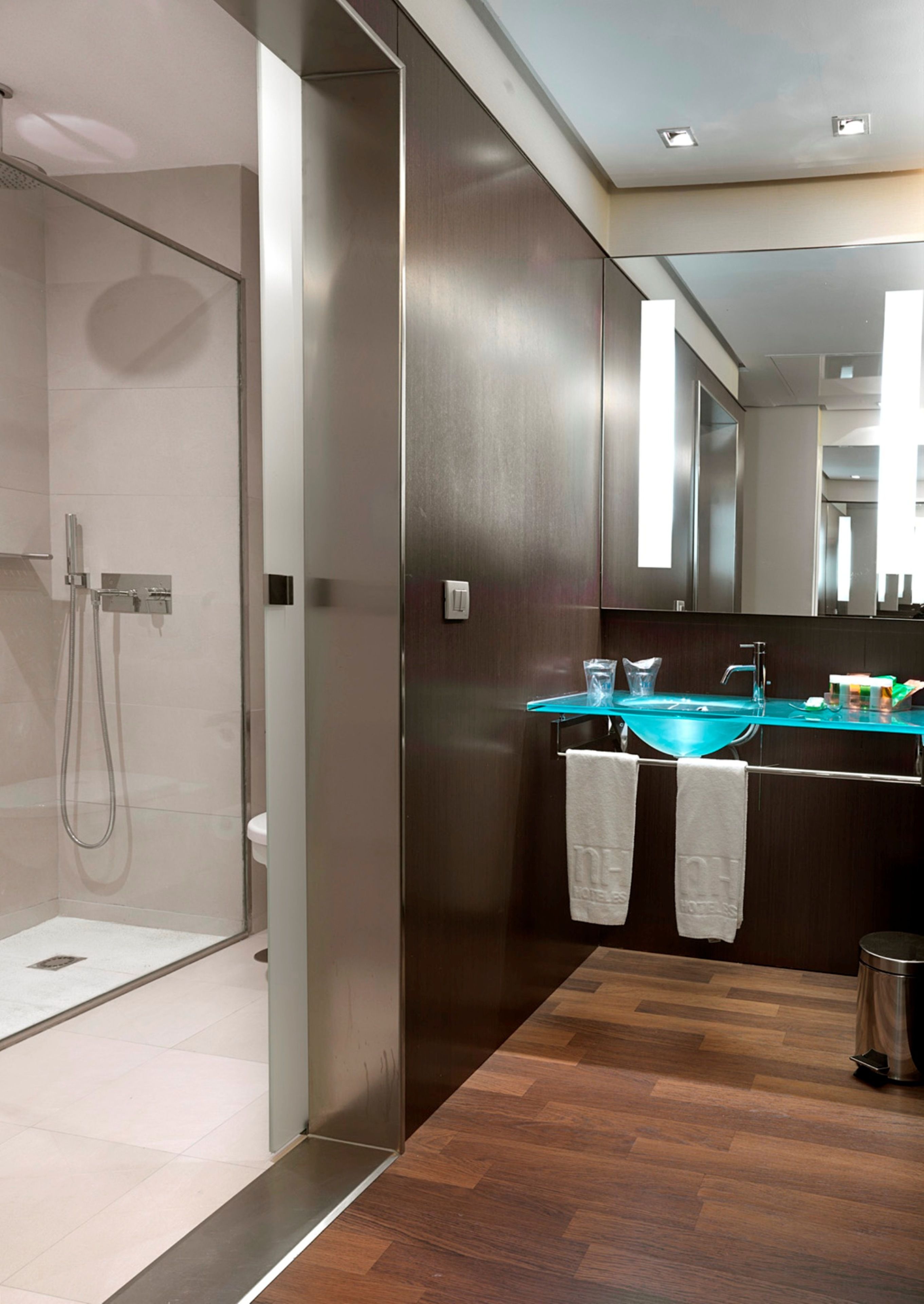 Un baño moderno con cabina de ducha de vidrio, lavamanos con encimera azul y suelo de madera.