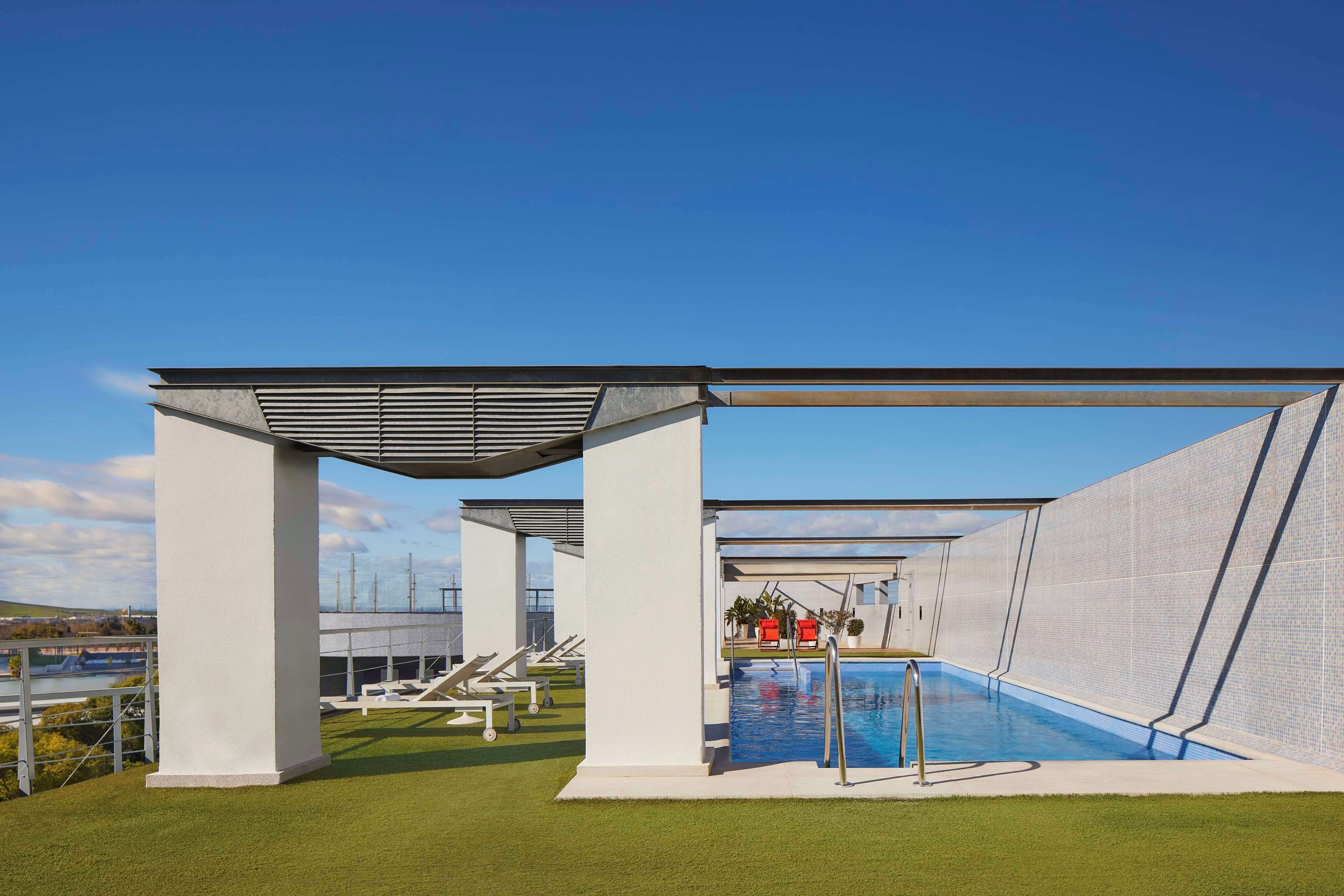A modern outdoor pool area with a clear blue sky, a pool, lounge chairs, and a covered seating area.