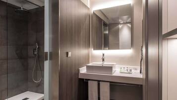 Un baño moderno con cabina de ducha de vidrio, tocador con espejo y suelo de madera.