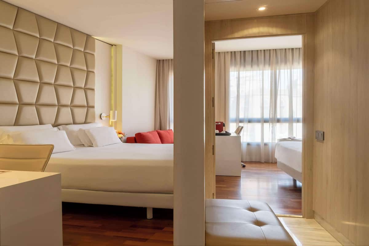 Una habitación de hotel moderna con una cama grande, un escritorio y vistas a la ciudad a través de amplios ventanales.