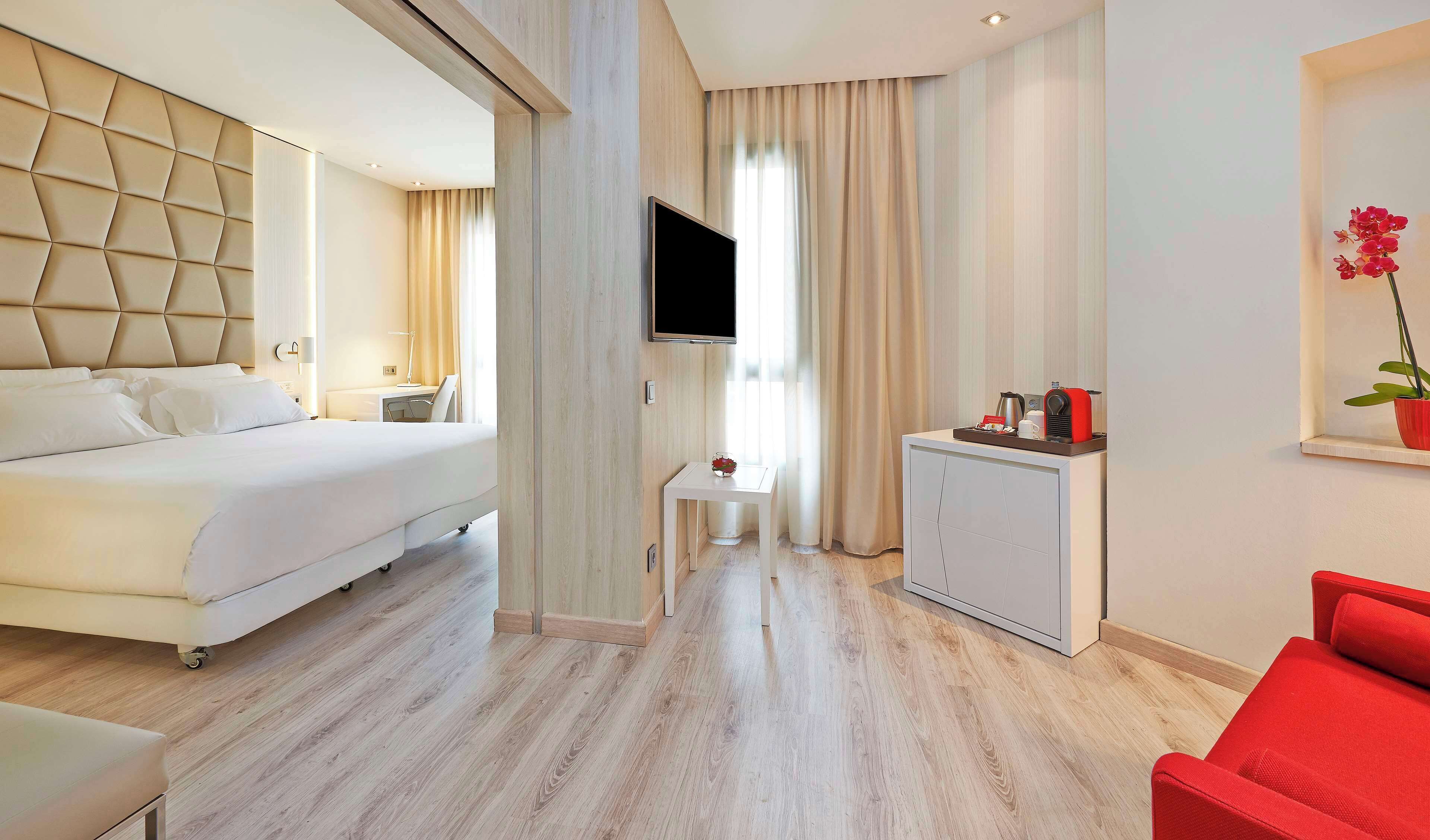 Una habitación de hotel con una cama, un escritorio, un televisor, una mesita pequeña, una silla roja y un armario.