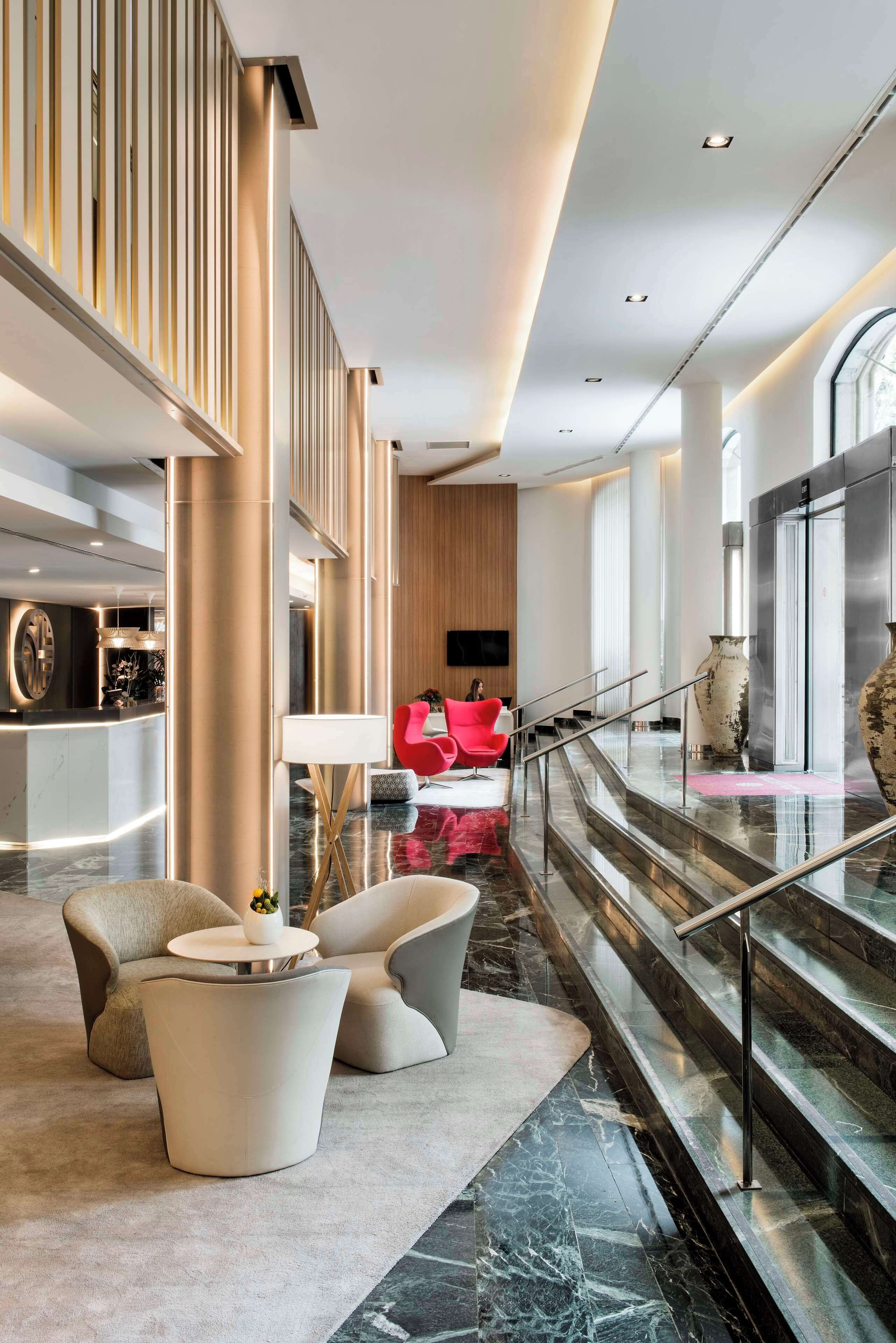 A modern lobby with a reception desk, seating area, and a staircase.