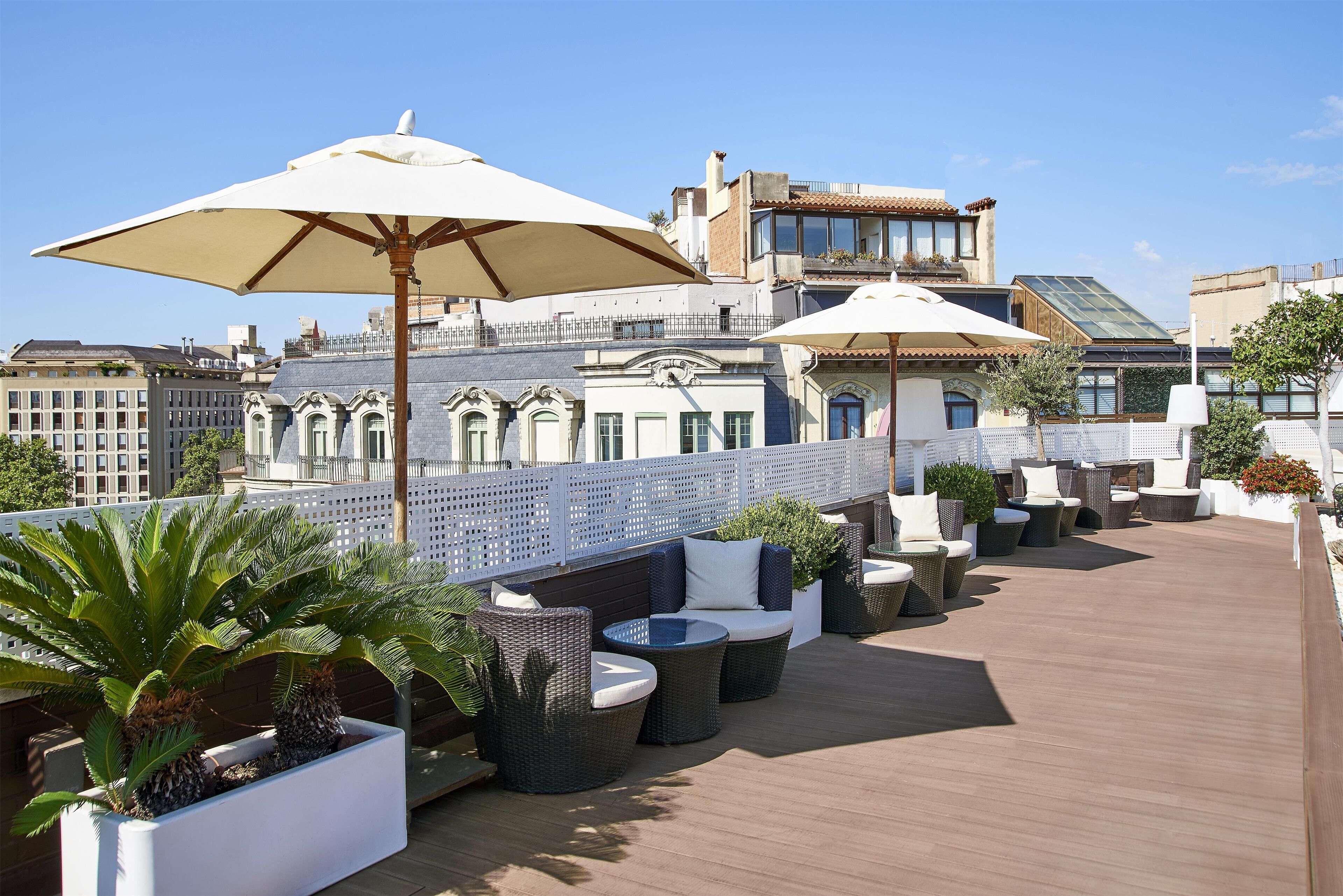 Una terraza en la azotea con mobiliario exterior, sombrillas grandes y plantas en macetas.