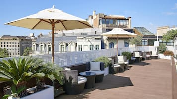 Una terraza en la azotea con mobiliario exterior, sombrillas grandes y plantas en macetas.