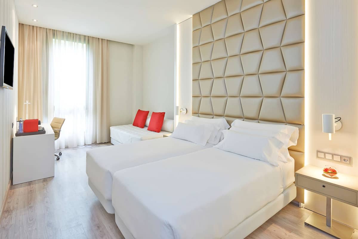 Habitación de hotel con dos camas, un escritorio, un televisor y un ventanal con cortinas.