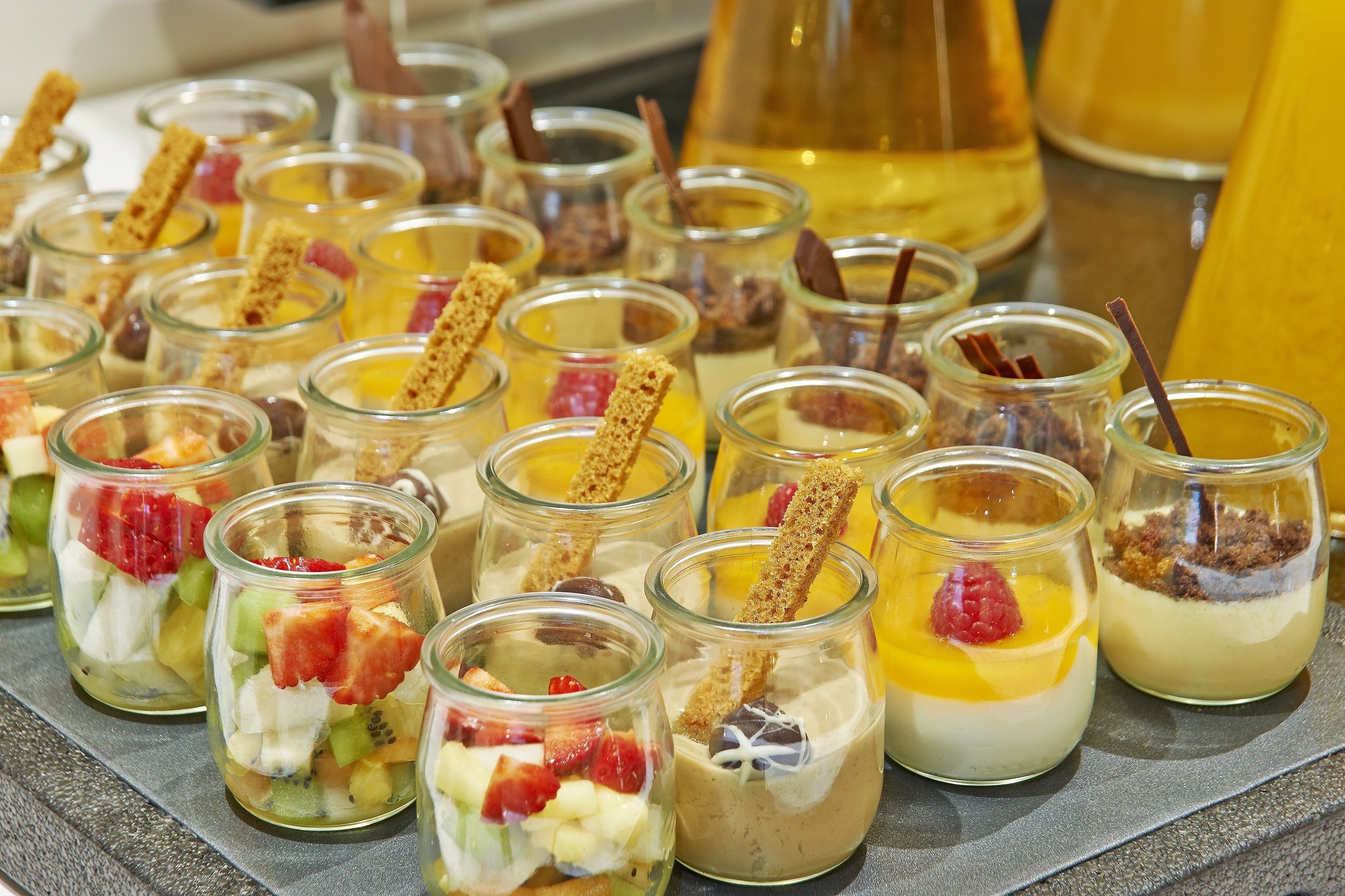 Verschiedene Dessertbecher mit unterschiedlichen Toppings und eine Flasche Sirup im Hintergrund.