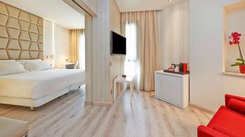 Une chambre d’hôtel moderne équipée d’un lit, d’un bureau, d’une télévision, d’une petite table ornée d’une fleur rouge et d’une chaise rouge.
