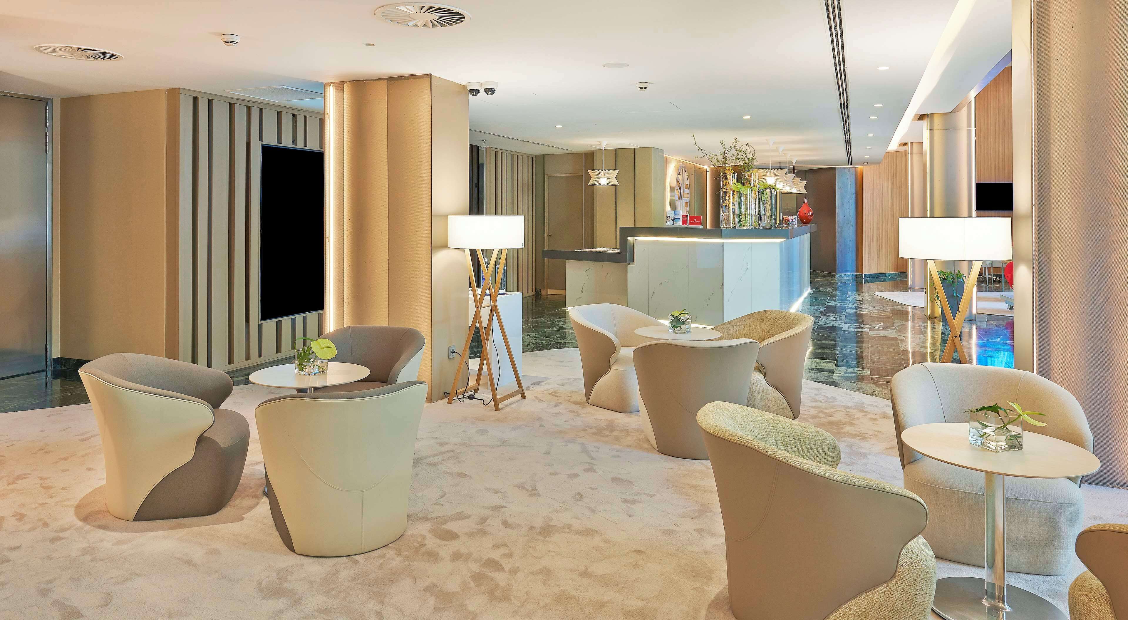A modern hotel lobby with contemporary furniture, a reception desk, and a view of the pool area.