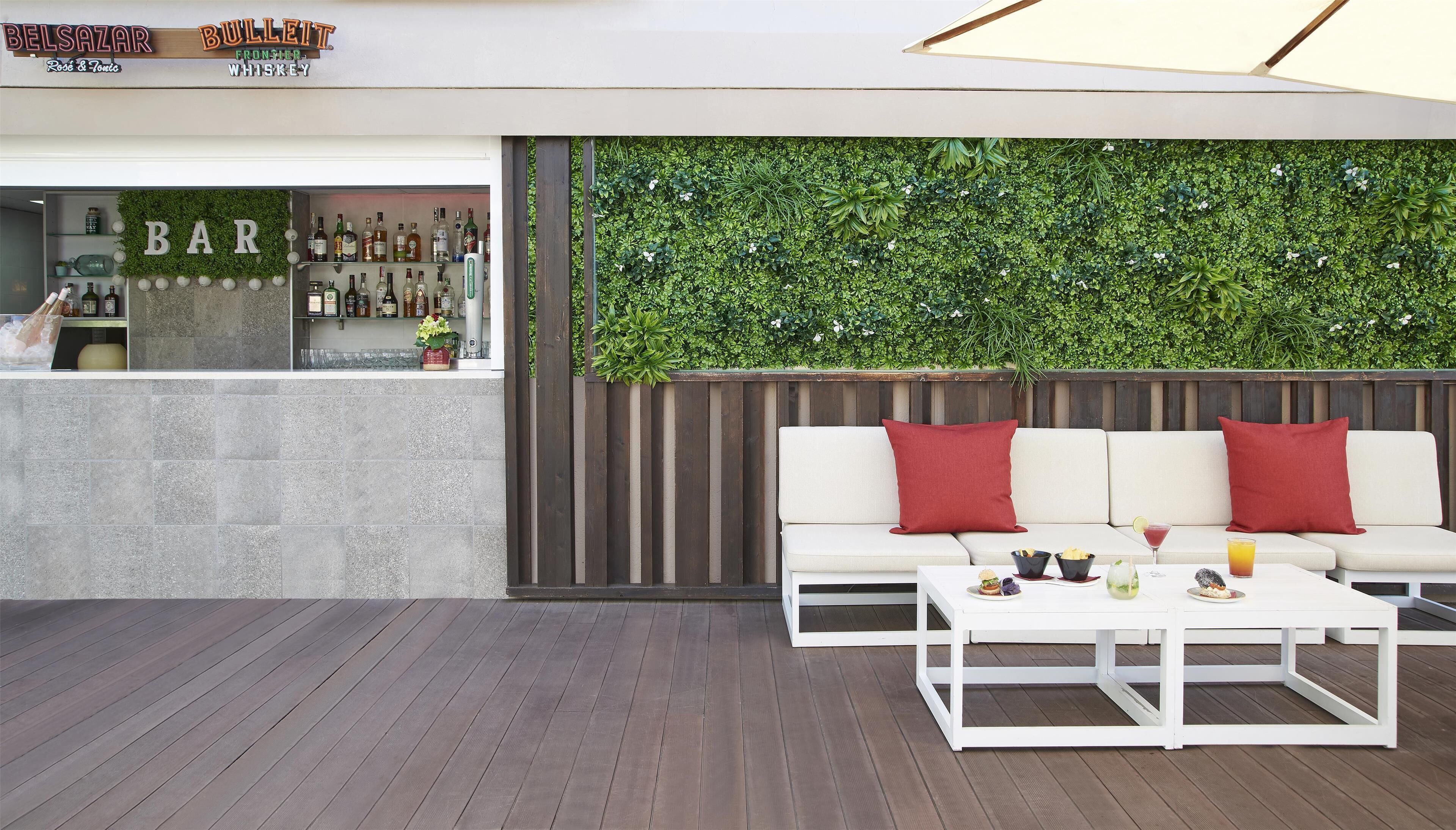 Un área de estar al aire libre con un sofá blanco y cojines rojos, una mesa de centro blanca y una barra con un fondo de pared verde.