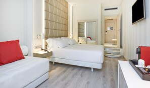 Habitació d'hotel amb un llit, una tauleta de nit i un coixí vermell.
