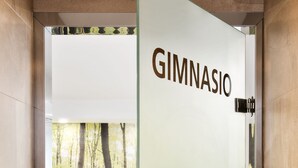 Der Eingang eines Fitnessstudios mit einer Tür mit der Aufschrift "GIMNASIO", einer Reihe von Kurzhanteln, einem Ergometer und einem großen Trainingsball.
