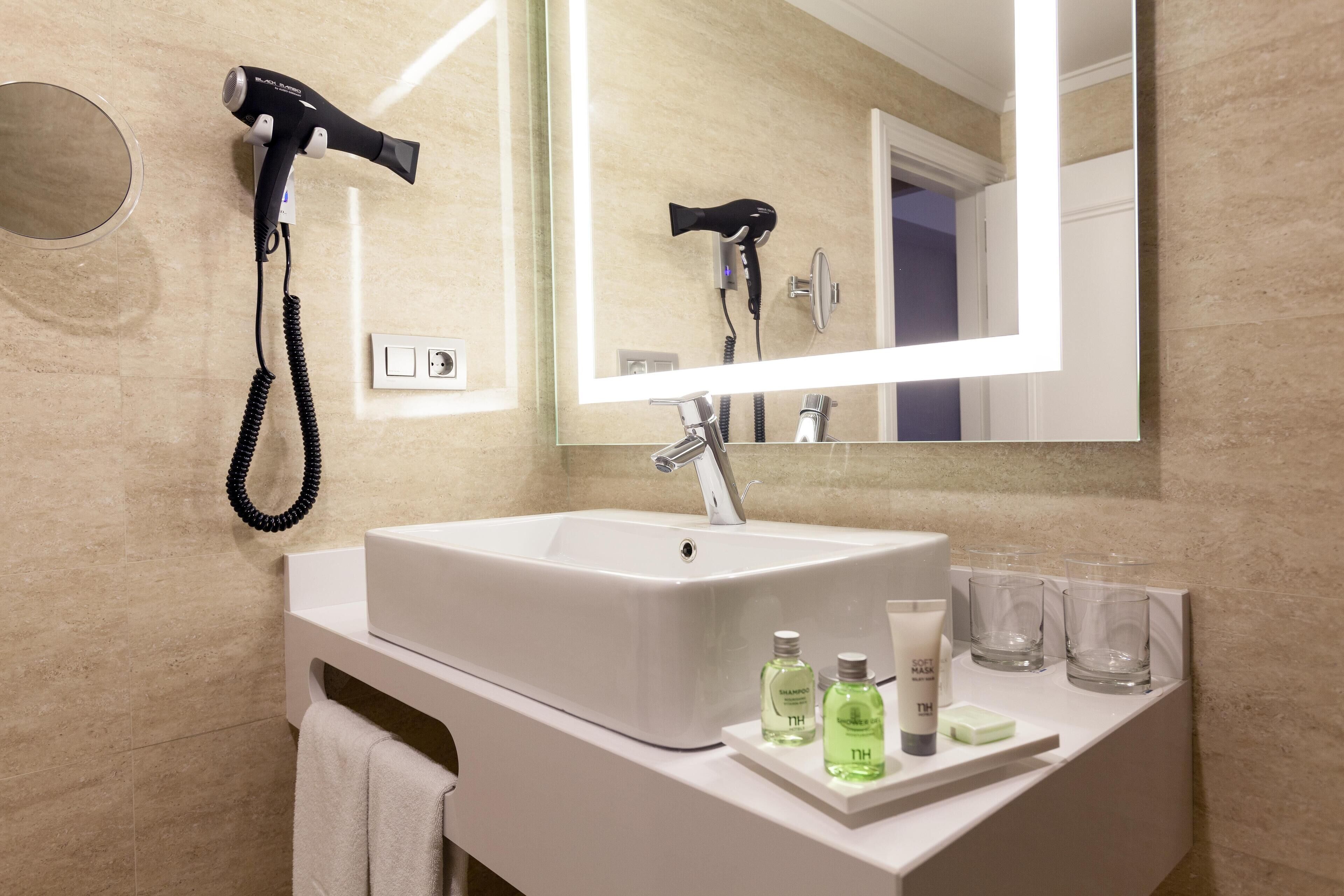 A modern bathroom with a large mirror, a white sink, and a hairdryer mounted on the wall.