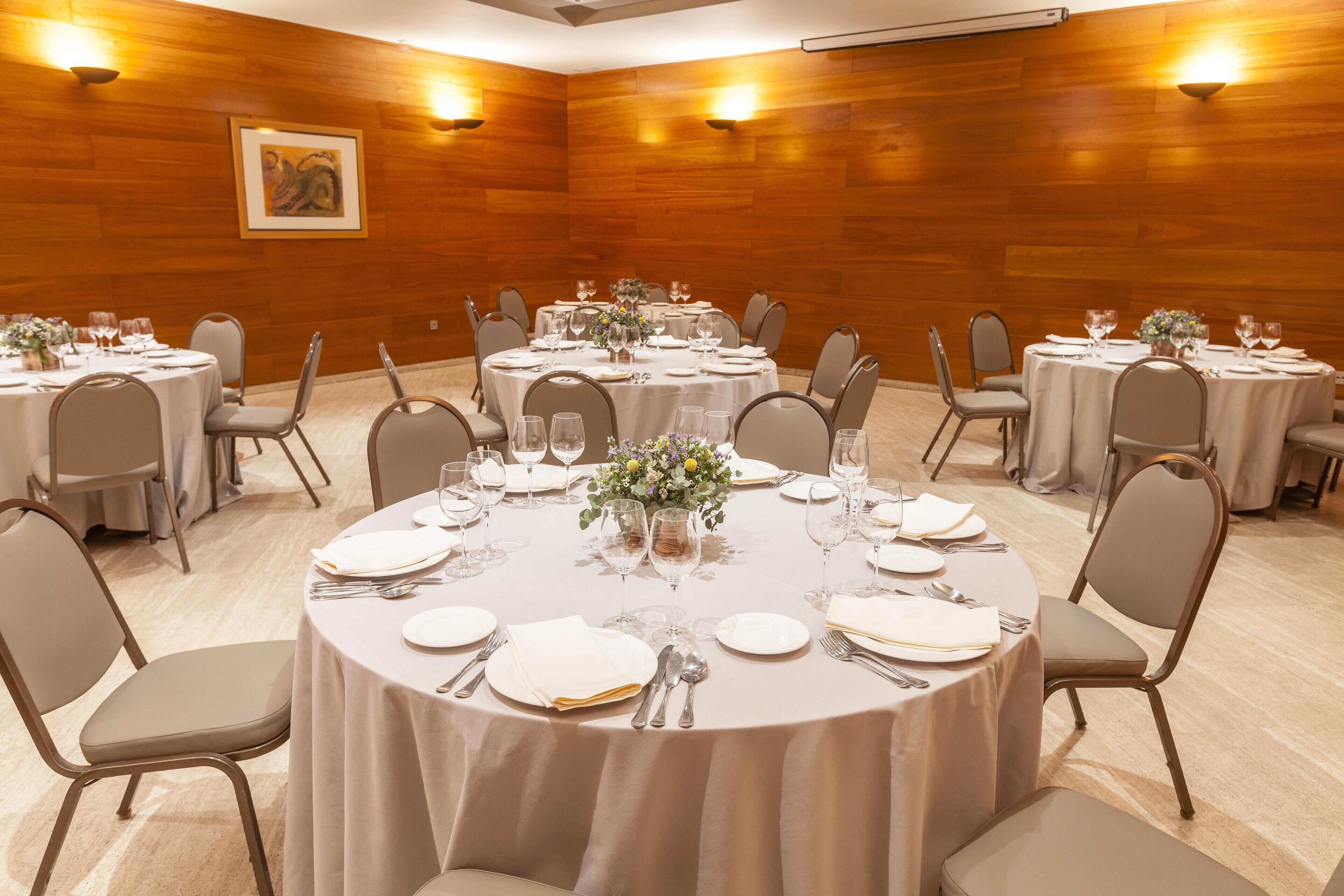 Un salón de conferencias con mesas redondas, sillas y un arreglo floral central.
