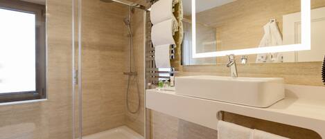 A modern bathroom with a glass-enclosed shower, a large mirror, and a white sink.