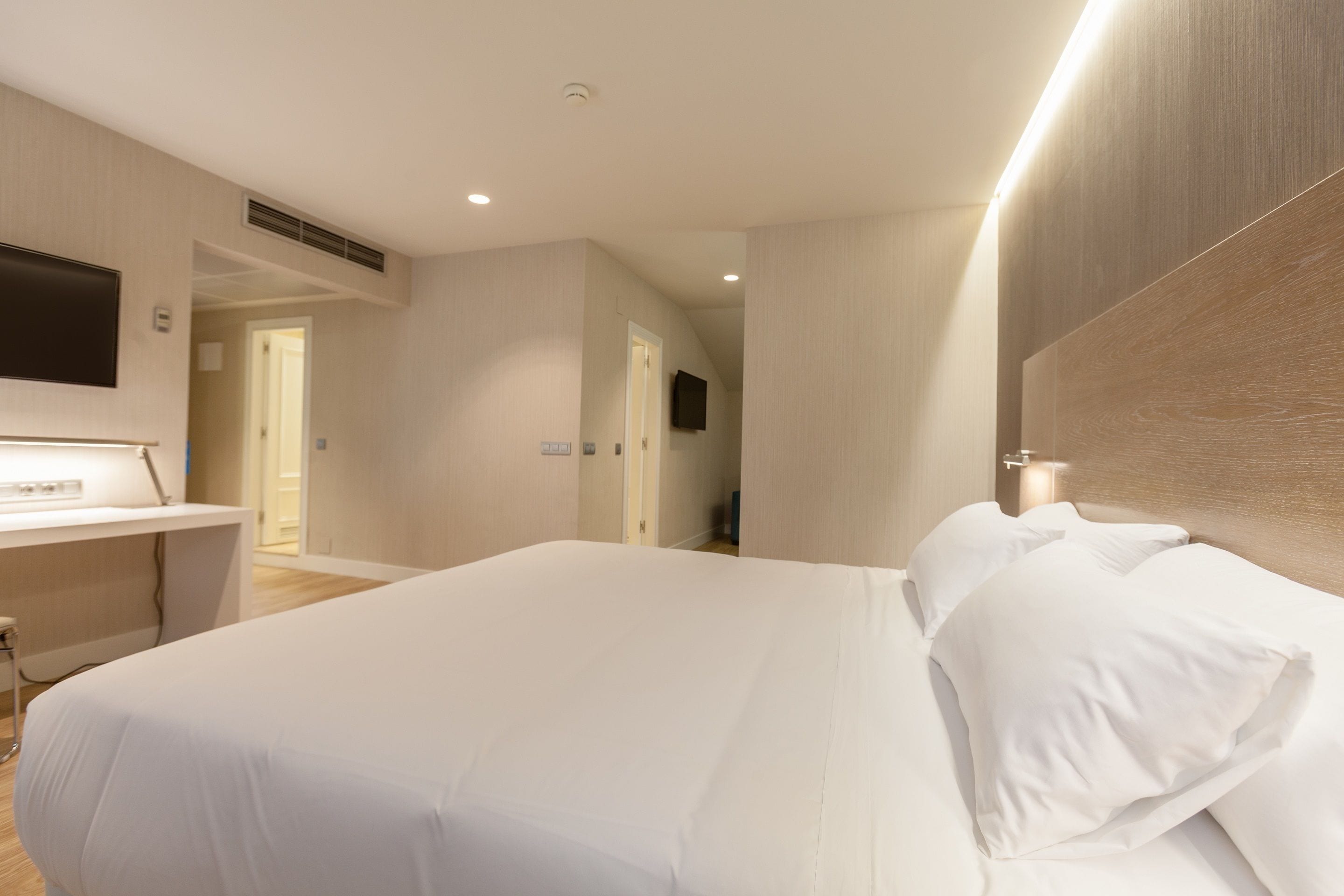A modern hotel room with a large bed, a desk, and a flat-screen TV mounted on the wall.