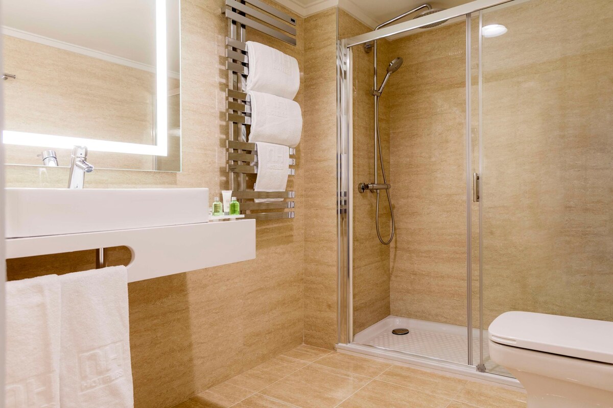 A modern bathroom with a glass-enclosed shower, a white sink with a mirror, and a towel rack with multiple towels.