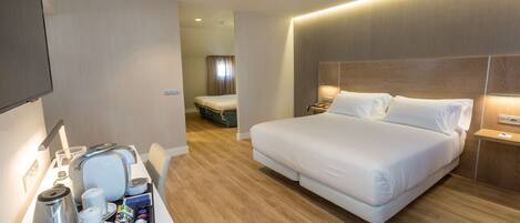A modern hotel room with a large bed, bedside tables, a desk with a tray of breakfast items, and a television.