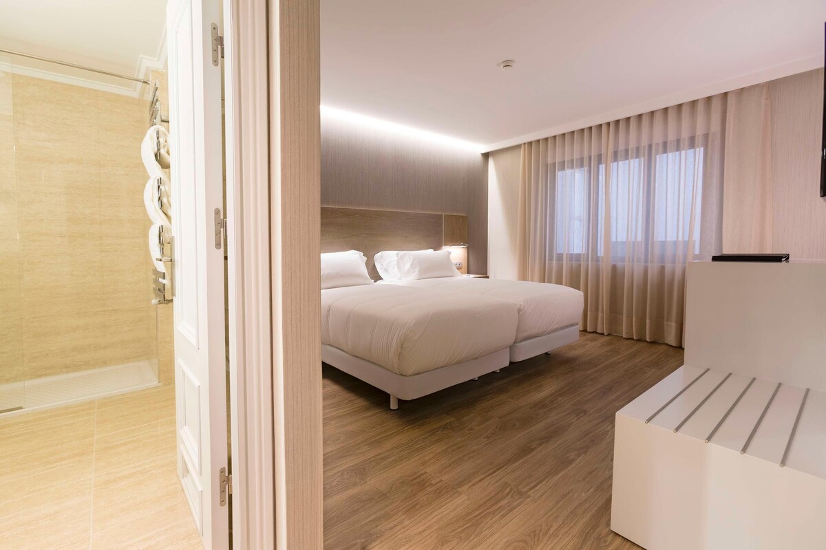 Ein modernes Hotelzimmer mit einem großen Bett, einem Nachttisch und einem Duschbereich.