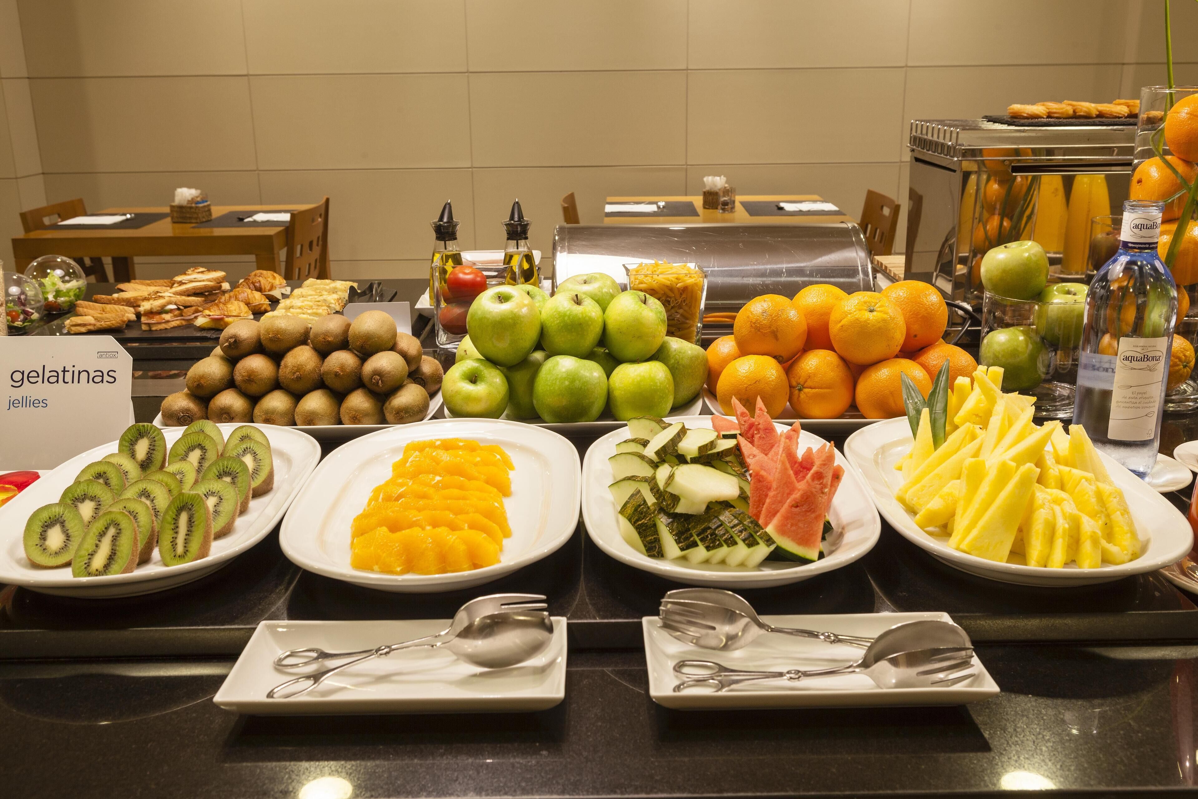 A buffet with various fruits and vegetables, including kiwi, oranges, and apples.