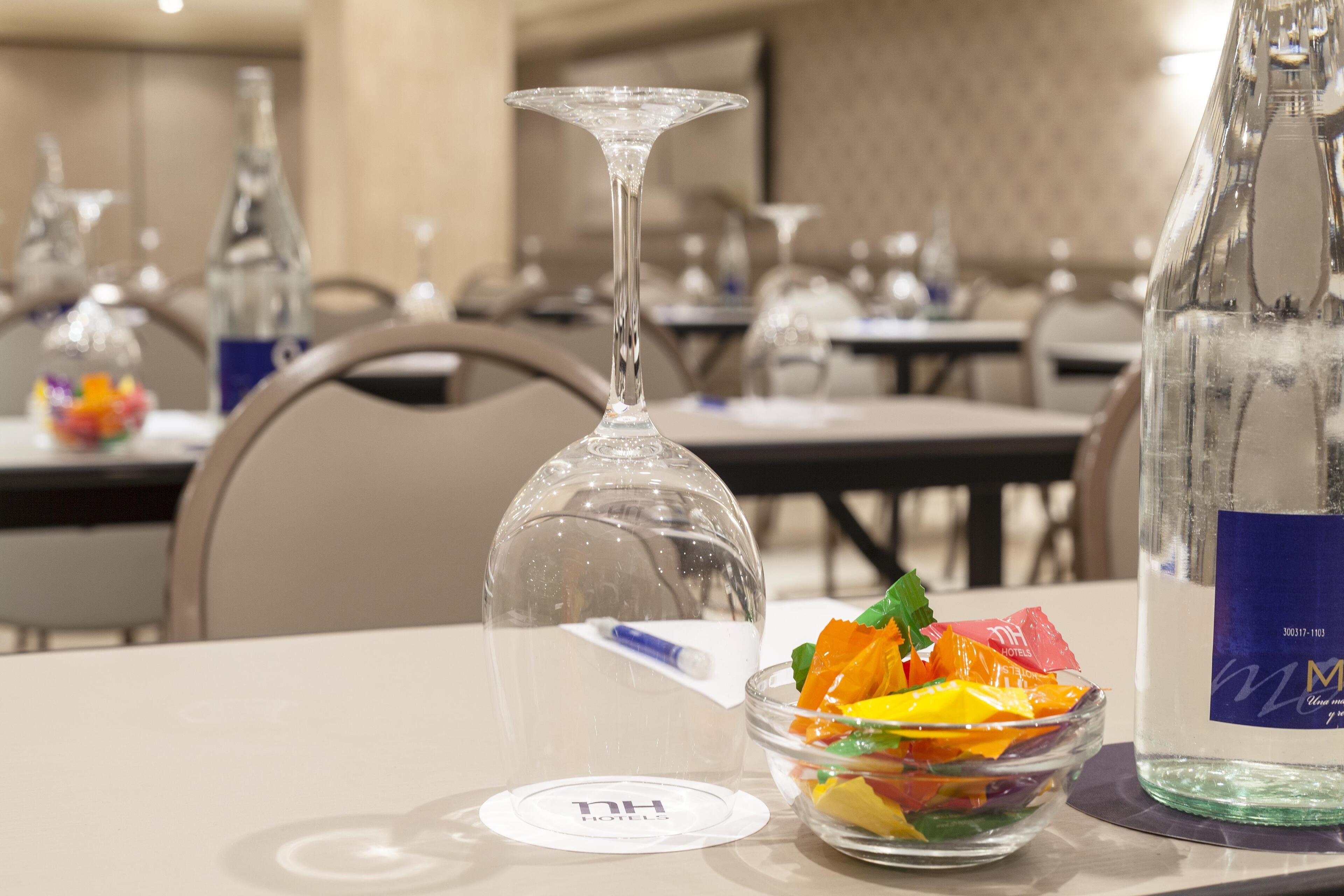 Una mesa de comedor con una copa de vino, un tazón de fruta colorida y una botella de agua.