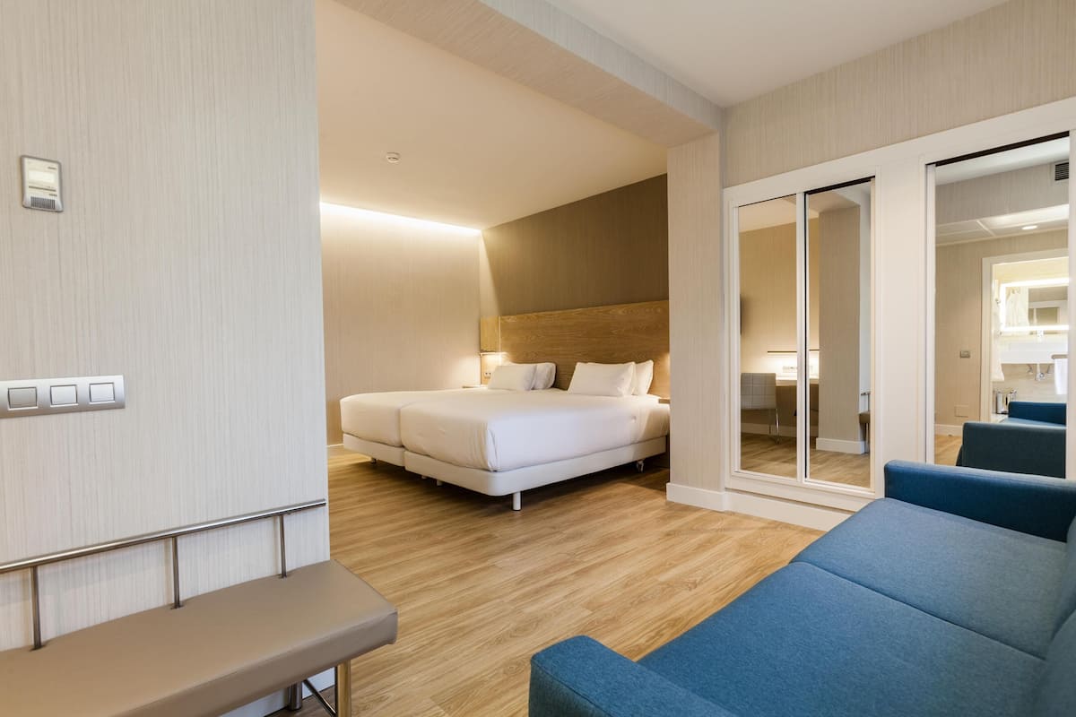 Ein modernes Hotelzimmer mit einem großen Bett, einer Sitzecke mit einer Bank und einer Schiebetür zu einem Badezimmer.