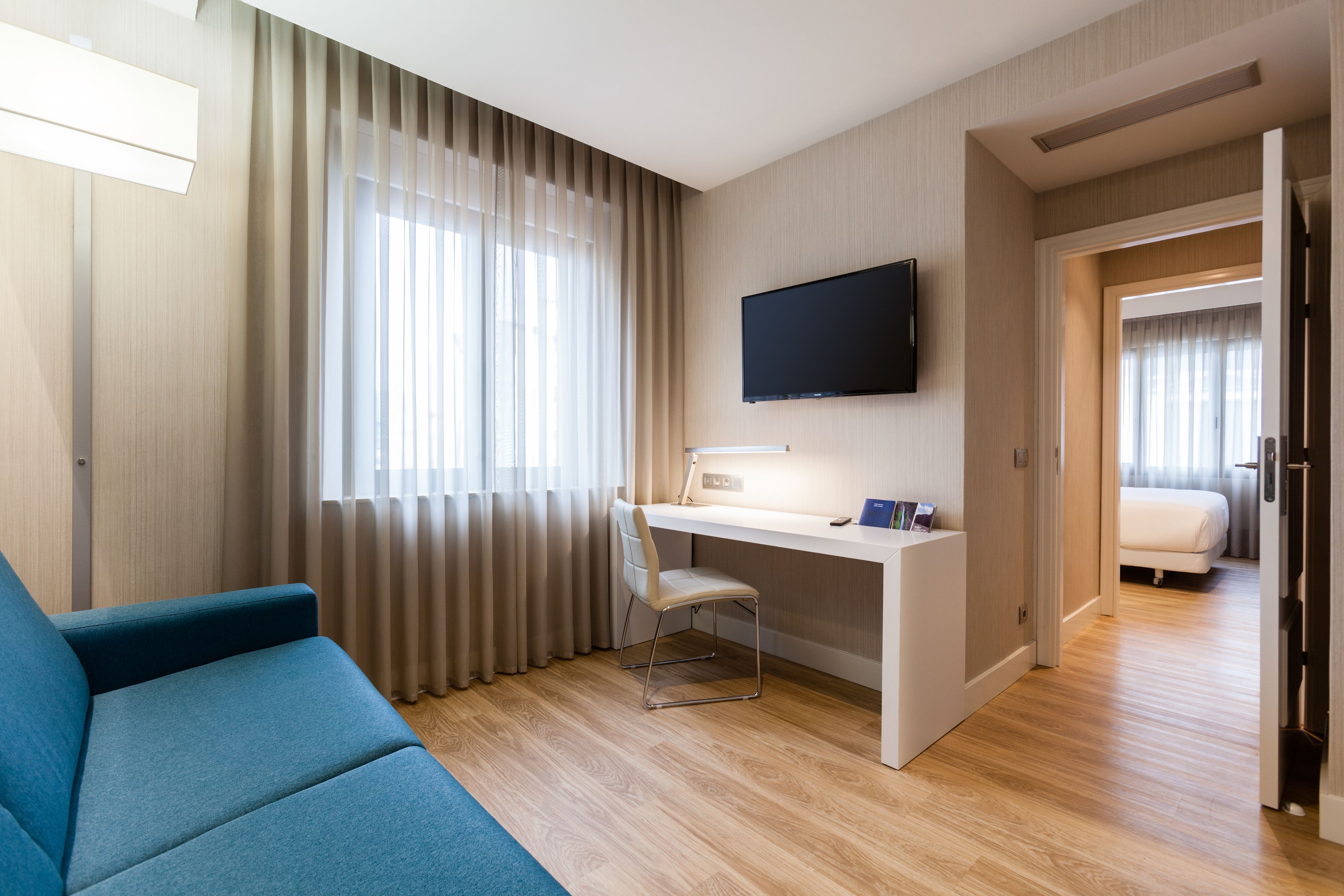 Una habitación de hotel moderna con un sofá azul, un escritorio con una computadora, un televisor de pantalla plana y una cama.