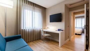 Una habitación de hotel moderna con un sofá azul, un escritorio con una computadora, un televisor de pantalla plana y una cama.