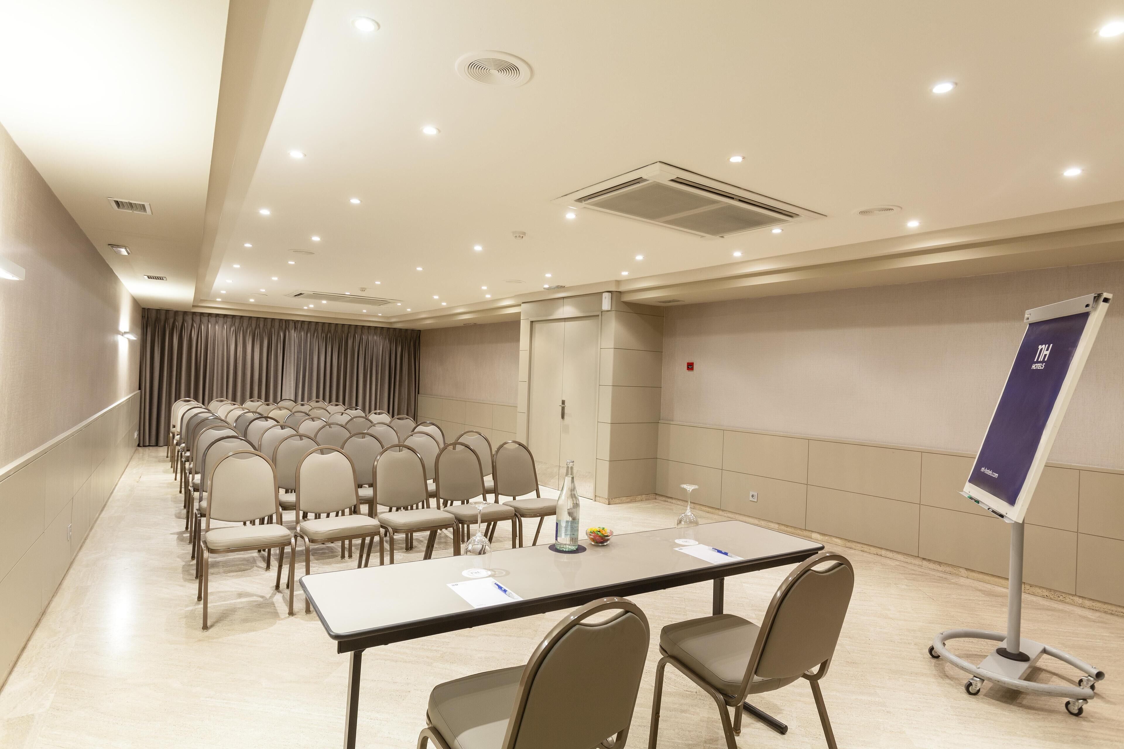 Un salón de conferencias con hileras de sillas, una mesa larga y un caballete.