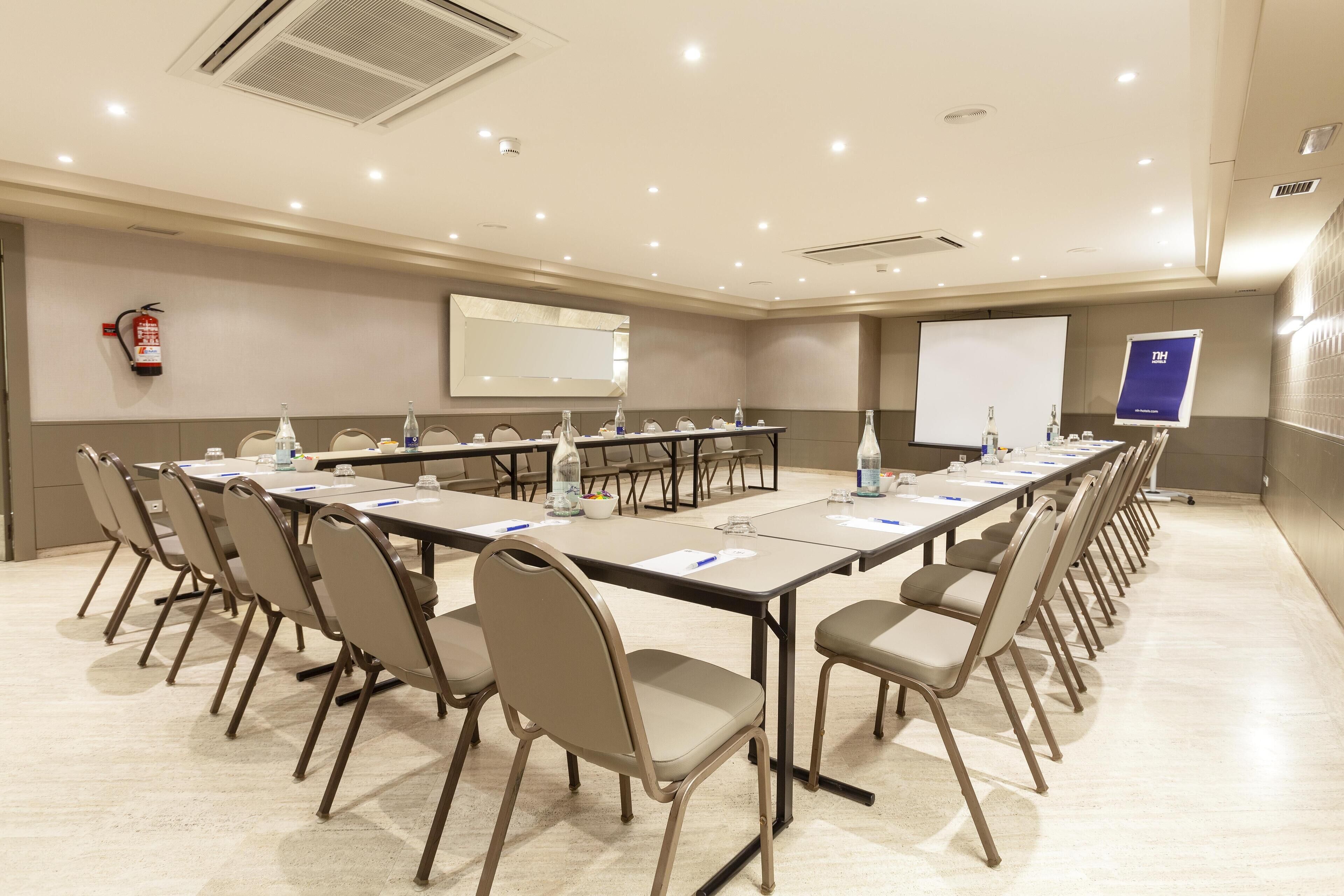 Un salón de conferencias con una larga mesa, sillas, una pantalla de proyector y un extintor.