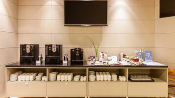 A breakfast bar with coffee machines, a flat-screen TV, and neatly arranged mugs and plates.