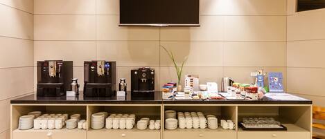 Una barra de desayuno con máquinas de café, un televisor de pantalla plana y tazas y platos ordenados.