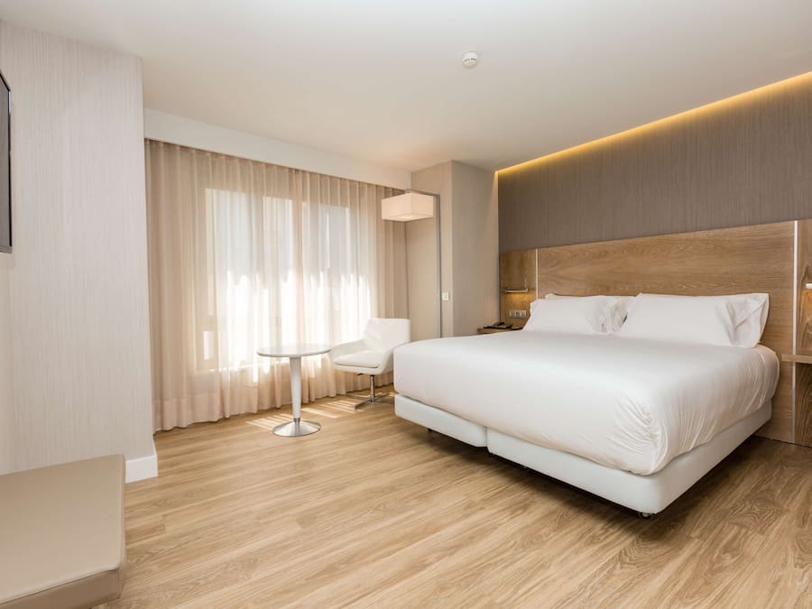 A modern hotel room with a large bed, a small table, a chair, and a TV mounted on the wall.