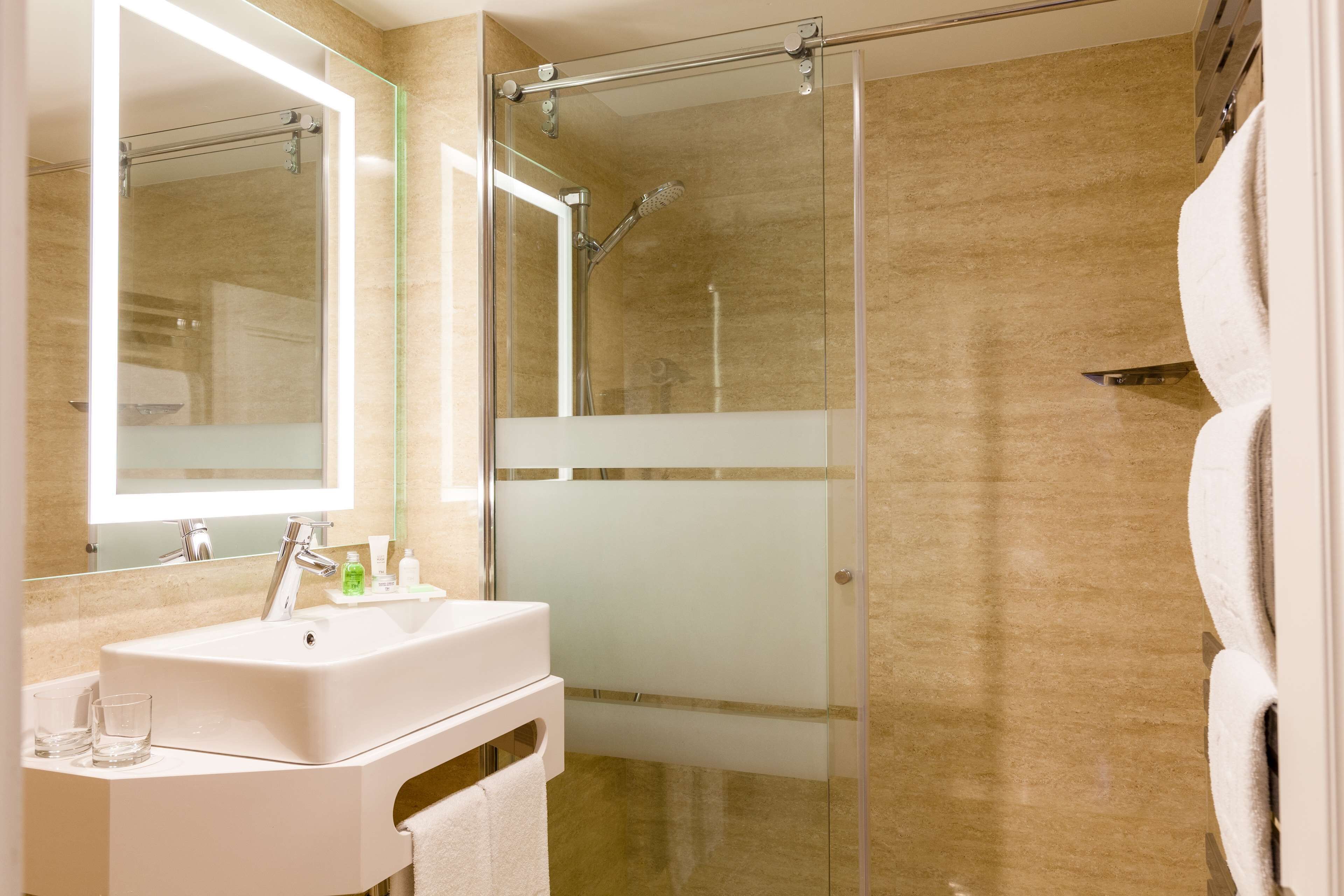 Un baño moderno con ducha de vidrio, lavamanos blanco con espejo y perchero.