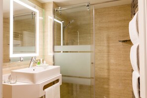 Un bany modern amb dutxa de vidre, un lavabo blanc amb mirall i un suport per tovalloles.