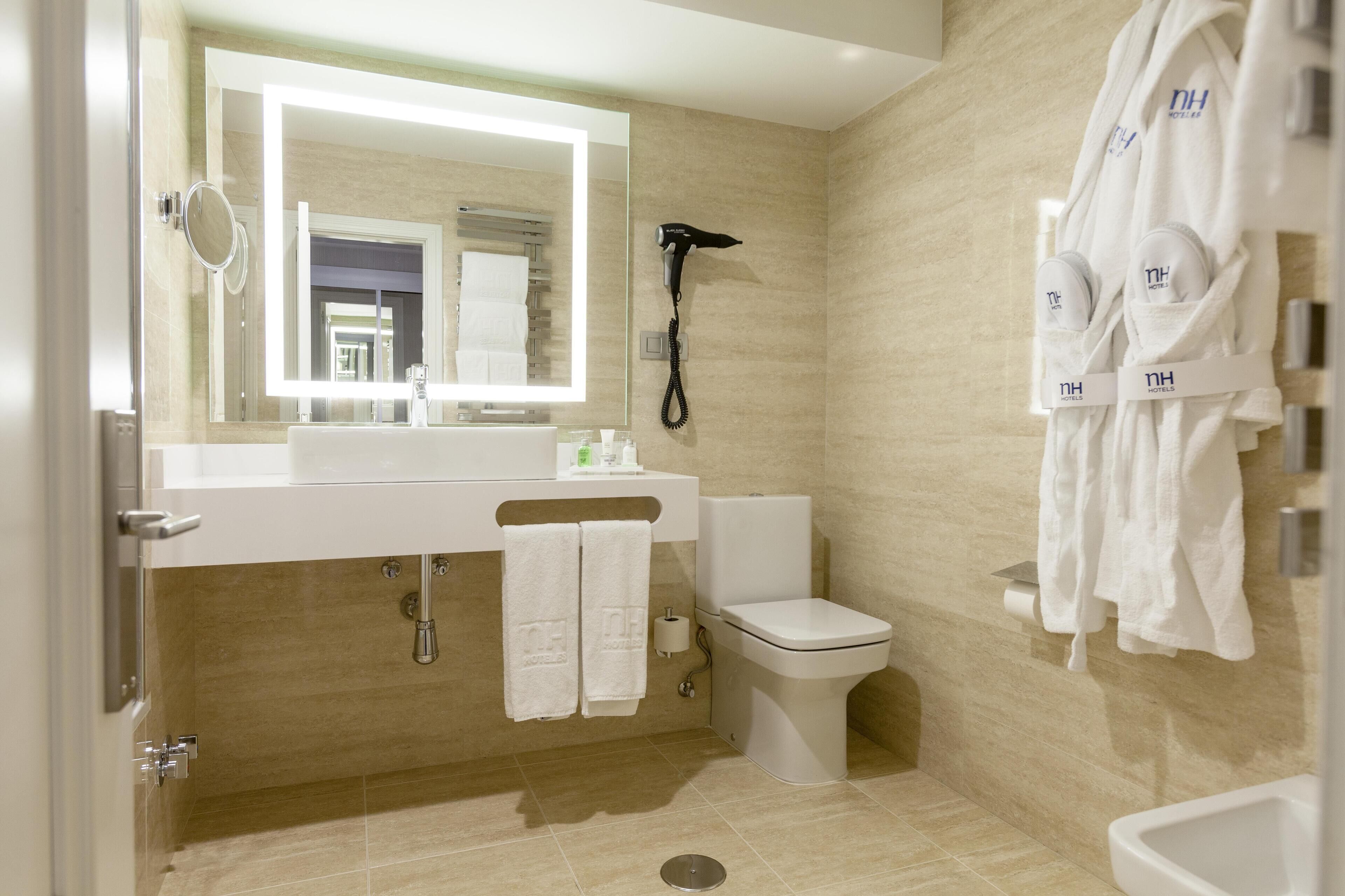 A modern bathroom with a large mirror, a hairdryer, a toilet, and a sink.