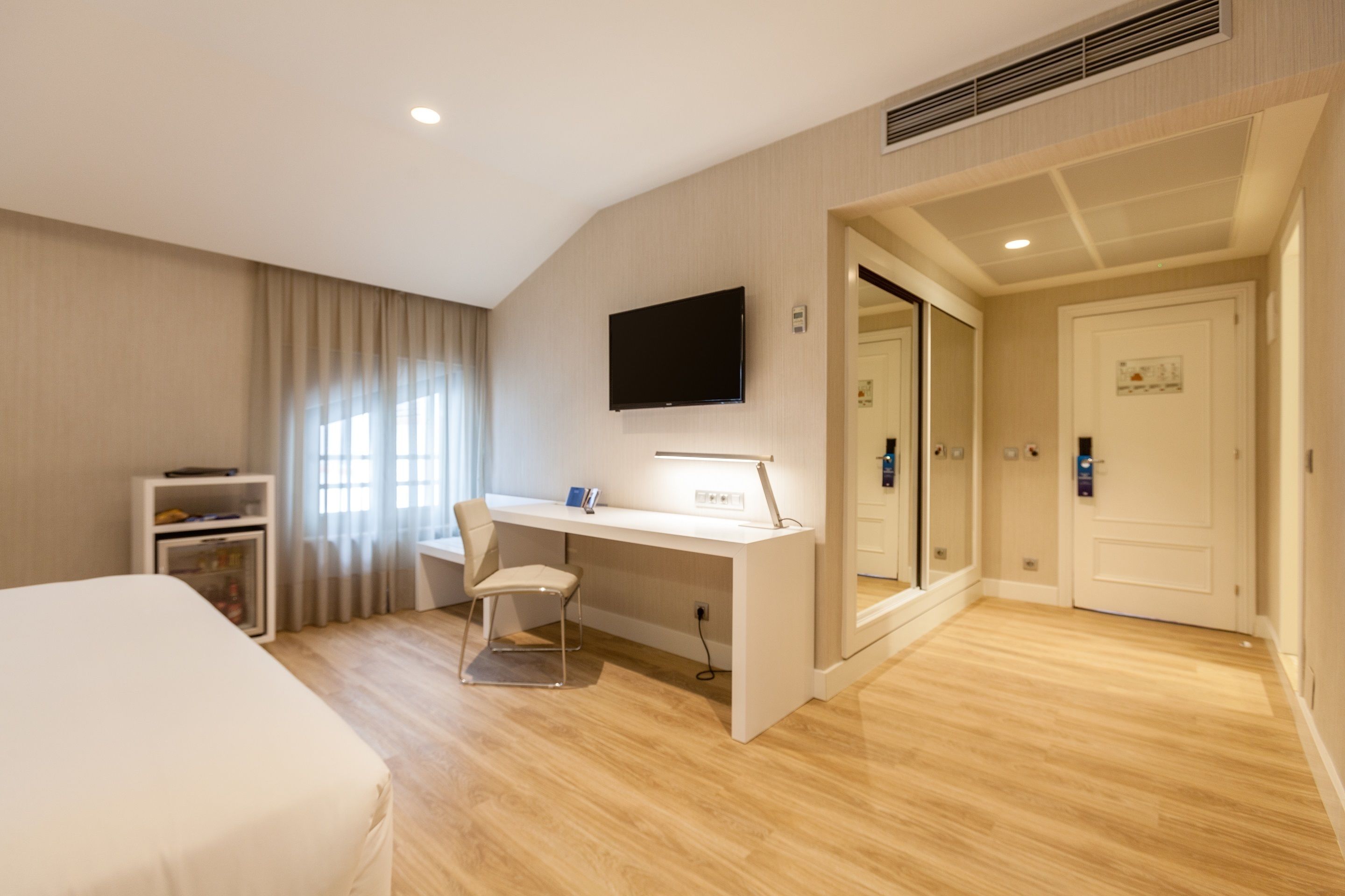 A hotel room with a bed, a desk with a chair, a television, and a door leading to another room.