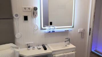 A modern bathroom with a white vanity, a mirror with LED lighting, a hairdryer, a phone, and a towel rack.