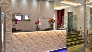 A hotel reception desk with a marble wall, a glass display case, and a blue-lit water feature. - Erase un Hotel (Madrid)