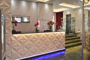 A hotel reception desk with a marble wall, a glass display case, and a blue-lit water feature.