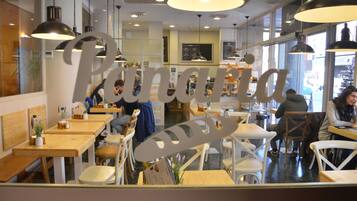 A restaurant interior with wooden tables and chairs, hanging pendant lights, and a menu board on the wall.